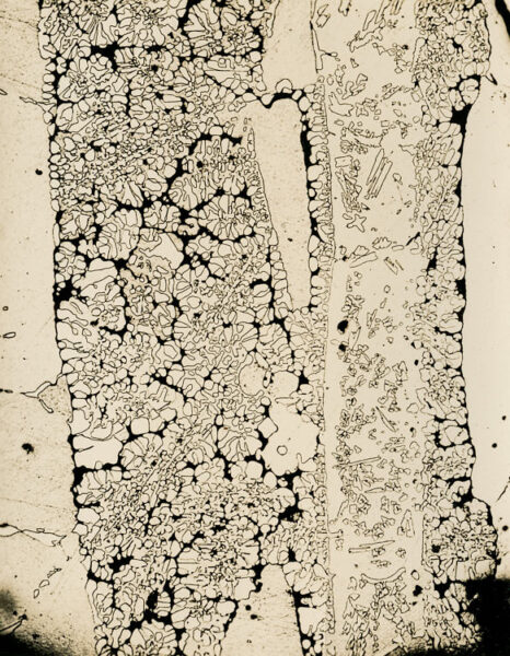 Photomicrograph of a molybdenum-carbide uranium alloy thin section, longitudinal, bottom-center, at 100x magnification, showing crystalline grain structure. Eldorado Nuclear Limited Metallographic Laboratory, 1968.